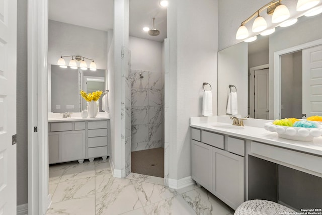 bathroom featuring marble finish floors, a marble finish shower, two vanities, and baseboards