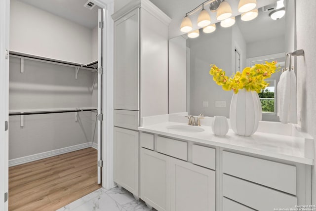 bathroom with vanity, marble look tiles, a spacious closet, and baseboards