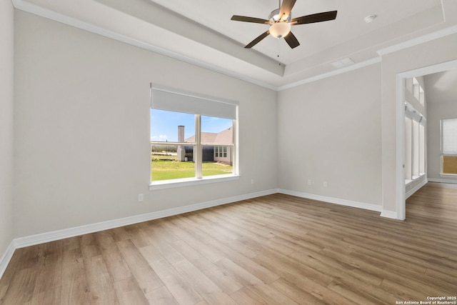 spare room with light wood finished floors, baseboards, a ceiling fan, a tray ceiling, and crown molding