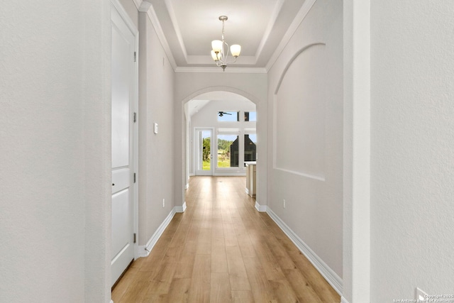 hall with arched walkways, a chandelier, light wood-type flooring, ornamental molding, and baseboards