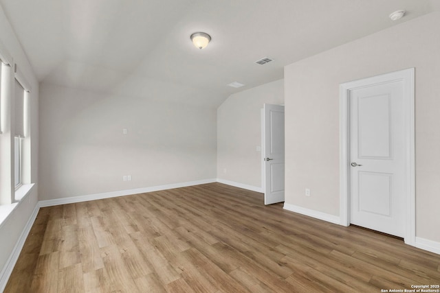 unfurnished room featuring light wood-type flooring, vaulted ceiling, a smoke detector, and baseboards