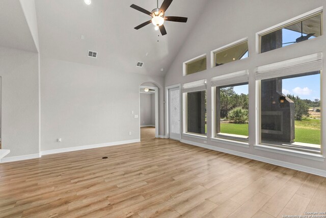 unfurnished living room with high vaulted ceiling, a ceiling fan, light wood-style floors, baseboards, and arched walkways