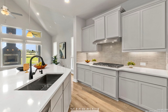 kitchen featuring a sink, under cabinet range hood, decorative backsplash, light countertops, and high vaulted ceiling