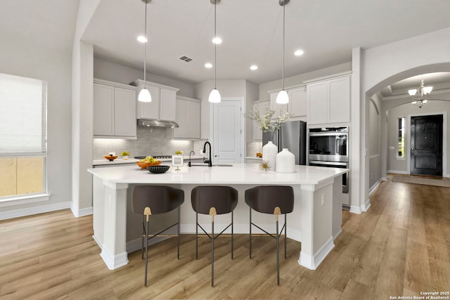 kitchen with under cabinet range hood, arched walkways, decorative backsplash, light countertops, and a sink