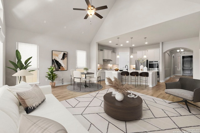 living area with arched walkways, light wood-style flooring, ceiling fan, high vaulted ceiling, and recessed lighting