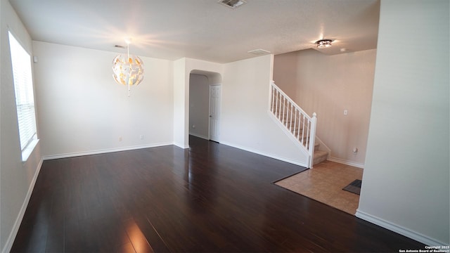 unfurnished living room featuring arched walkways, stairway, wood finished floors, a chandelier, and baseboards