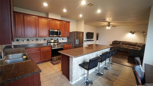 kitchen featuring stainless steel appliances, a kitchen breakfast bar, a sink, open floor plan, and dark countertops