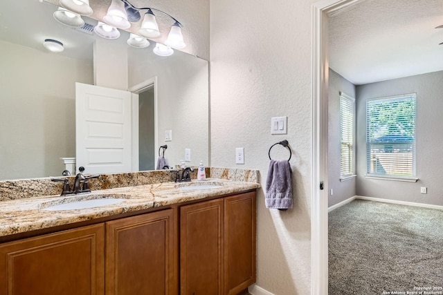 bathroom with double vanity, a textured wall, and baseboards