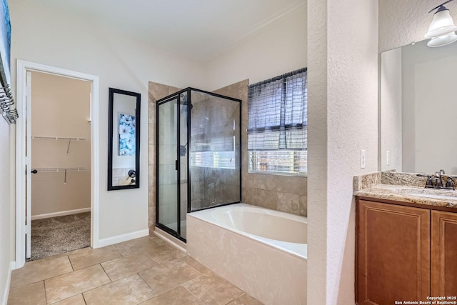 bathroom with a shower stall, a textured wall, a garden tub, a walk in closet, and vanity