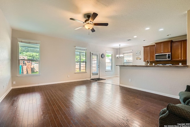unfurnished living room with a sink, ceiling fan, a chandelier, baseboards, and dark wood-type flooring