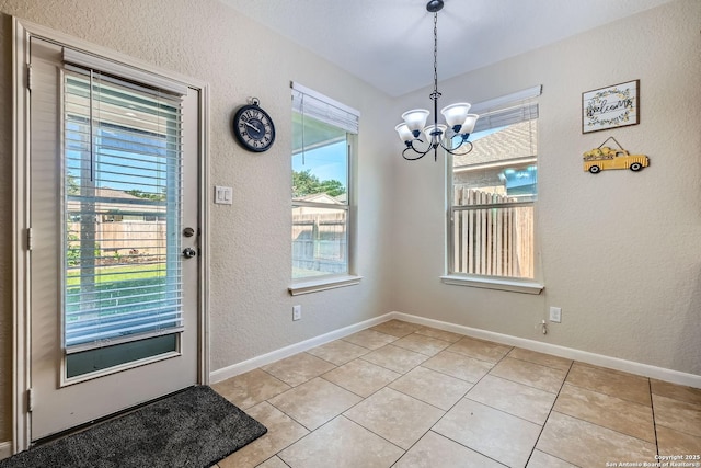 doorway to outside with a chandelier, a textured wall, light tile patterned flooring, and baseboards