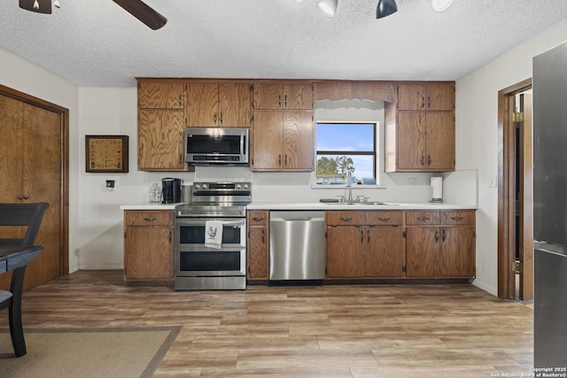 2050 Adj Ln, Fredericksburg, TX 78624 - kitchen with stainless steel appliances, a sink, a textured ceiling, light wood-type flooring, and brown cabinetry