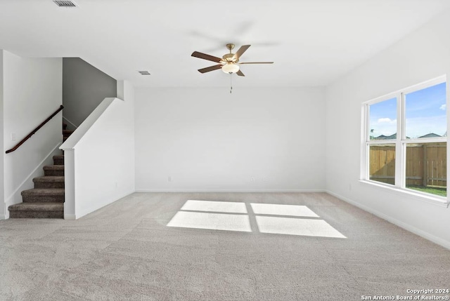 unfurnished living room featuring carpet flooring, a ceiling fan, stairs, and baseboards