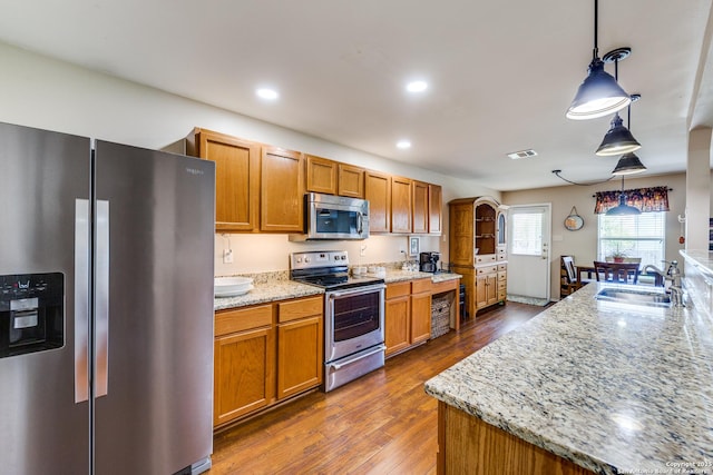 kitchen with stainless steel appliances, a sink, dark wood-style floors, brown cabinetry, and recessed lighting