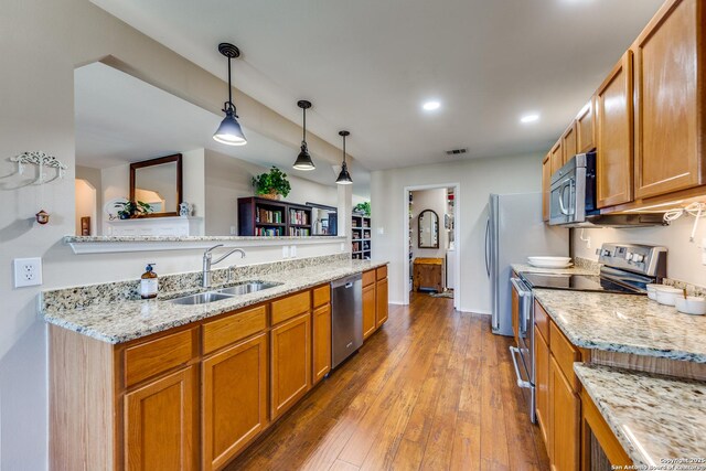 kitchen featuring stainless steel appliances, a sink, brown cabinetry, pendant lighting, and hardwood / wood-style flooring