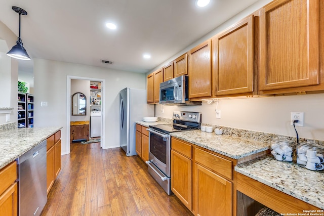 kitchen featuring appliances with stainless steel finishes, wood finished floors, recessed lighting, pendant lighting, and light stone counters