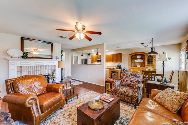living area featuring ceiling fan, wood finished floors, a fireplace, and baseboards