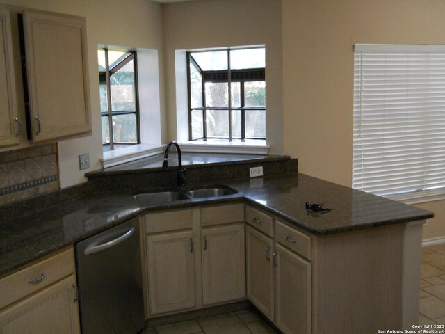 kitchen featuring dishwasher, a sink, a peninsula, light tile patterned floors, and dark stone counters