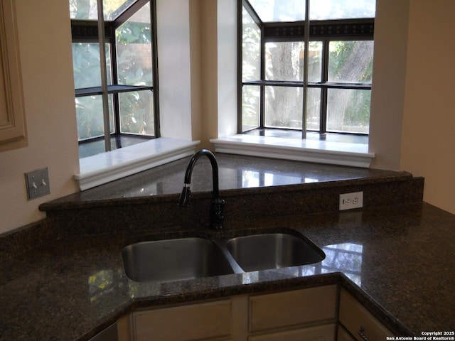 kitchen with a sink, healthy amount of natural light, dark stone counters, and white cabinetry