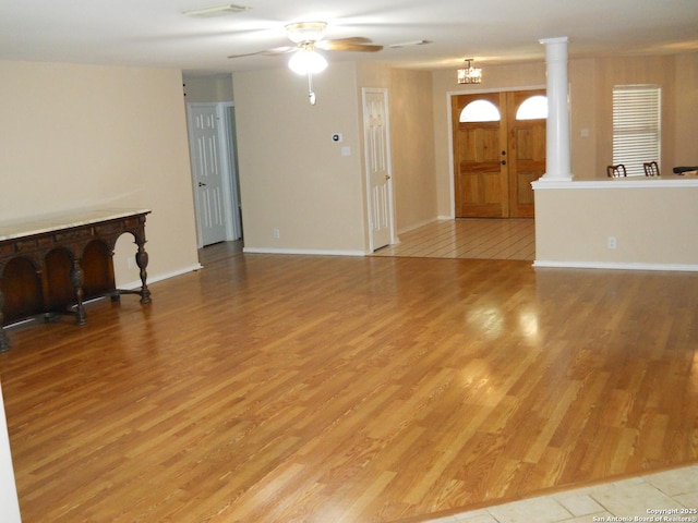 unfurnished living room featuring wood finished floors, a ceiling fan, baseboards, and decorative columns
