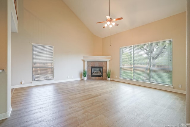 unfurnished living room with high vaulted ceiling, a ceiling fan, wood finished floors, a fireplace, and baseboards