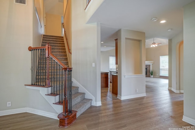 stairs featuring ceiling fan, wood finished floors, a fireplace, baseboards, and recessed lighting