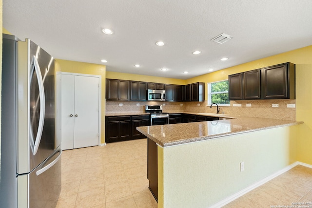 7923 Martinelli, San Antonio, TX 78253 - kitchen featuring appliances with stainless steel finishes, a peninsula, tasteful backsplash, dark brown cabinetry, and light stone countertops