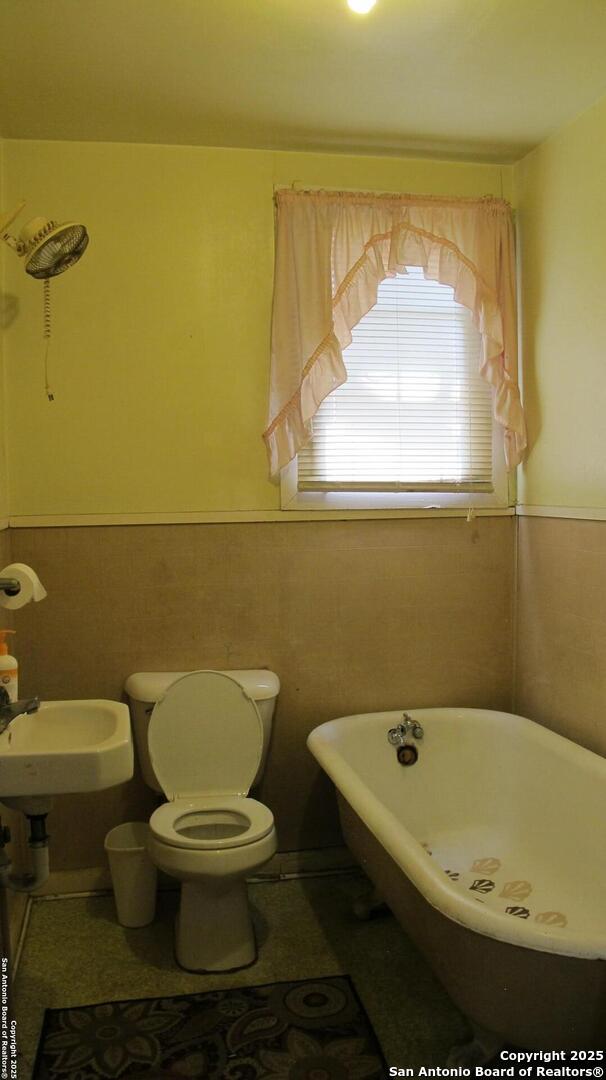2222 Osburn, San Antonio, TX 78208 - bathroom featuring a soaking tub, wainscoting, toilet, and tile walls