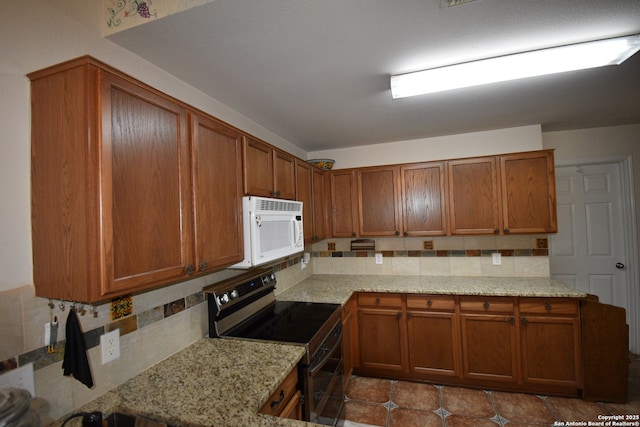 kitchen with electric range, white microwave, backsplash, and brown cabinets