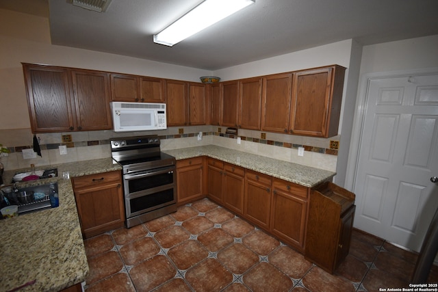 kitchen featuring range with two ovens, white microwave, tasteful backsplash, brown cabinetry, and light stone countertops