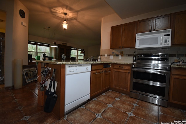 kitchen with white appliances, a peninsula, lofted ceiling, dark tile patterned flooring, and brown cabinets