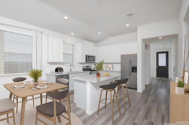 kitchen with stainless steel appliances, a center island, light wood-type flooring, backsplash, and lofted ceiling