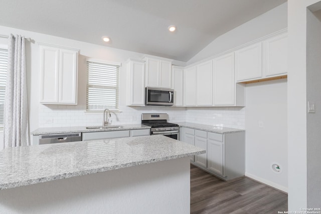 kitchen with appliances with stainless steel finishes, a sink, tasteful backsplash, dark wood-style floors, and light stone counters