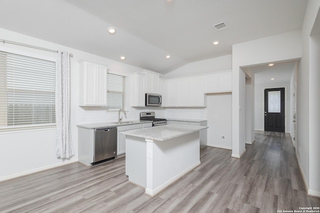 kitchen with stainless steel appliances, a sink, light wood-type flooring, decorative backsplash, and a center island