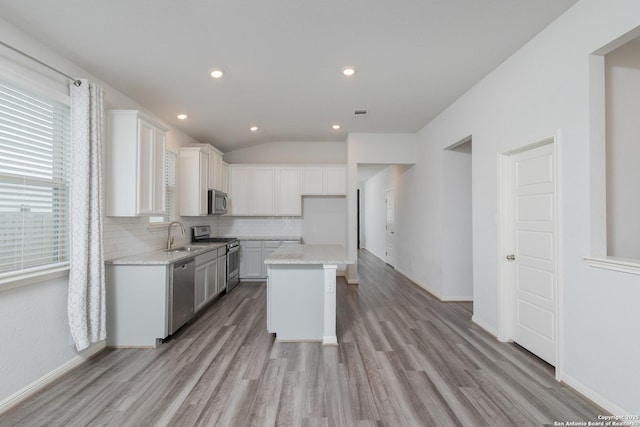 kitchen featuring appliances with stainless steel finishes, light wood-style floors, backsplash, white cabinets, and lofted ceiling