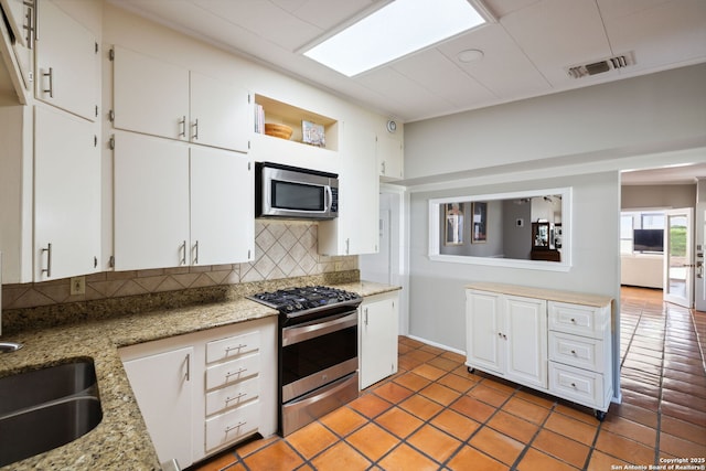 7214 N Vandiver, San Antonio, TX 78209 - kitchen with stainless steel appliances, decorative backsplash, white cabinets, light stone counters, and a sink