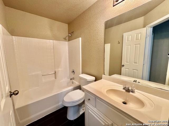 full bath with a textured wall, toilet, a textured ceiling, tub / shower combination, and vanity