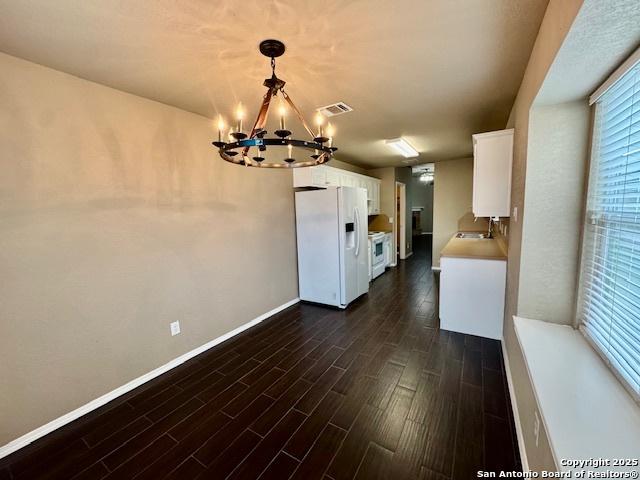 unfurnished dining area with a chandelier, dark wood finished floors, and baseboards