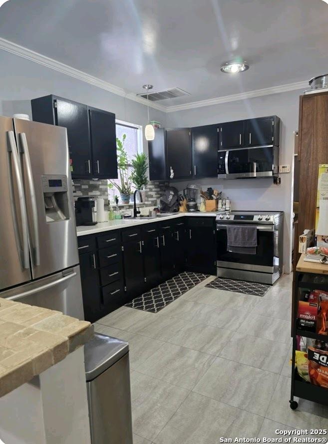 Schertz, TX 78154 - kitchen featuring appliances with stainless steel finishes, dark cabinets, a sink, crown molding, and decorative backsplash