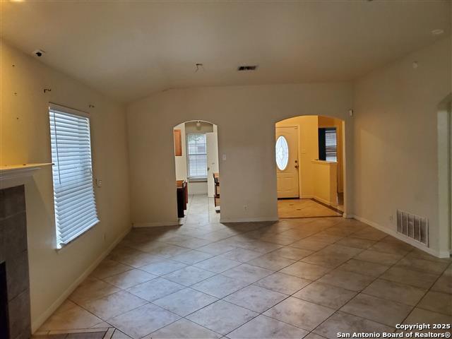 4218 Swan Frst, San Antonio, TX 78222 - unfurnished living room with arched walkways, light tile patterned floors, a tiled fireplace, vaulted ceiling, and baseboards