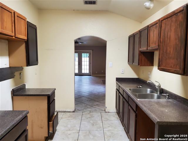 4218 Swan Frst, San Antonio, TX 78222 - kitchen featuring a sink, arched walkways, lofted ceiling, dark countertops, and light tile patterned floors