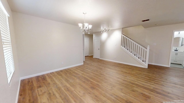 empty room featuring stairway, a chandelier, light wood-type flooring, baseboards, and a sink