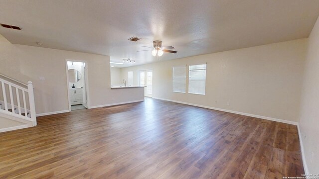 unfurnished living room with ceiling fan, stairs, wood finished floors, and baseboards