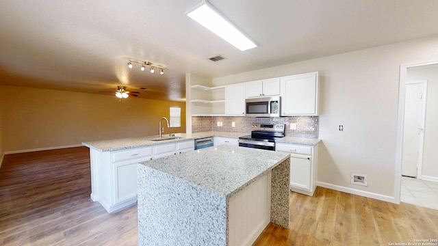 kitchen featuring appliances with stainless steel finishes, open shelves, a peninsula, a sink, and tasteful backsplash