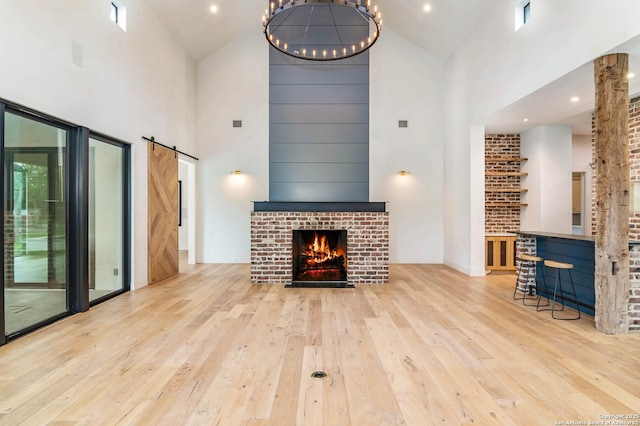 185 Southfield, Boerne, TX 78006 - unfurnished living room with high vaulted ceiling, wood-type flooring, a brick fireplace, and a barn door