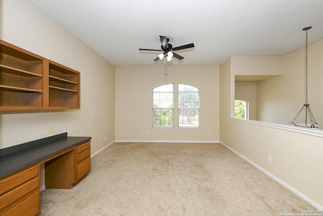 unfurnished office with built in desk, ceiling fan, light colored carpet, and baseboards