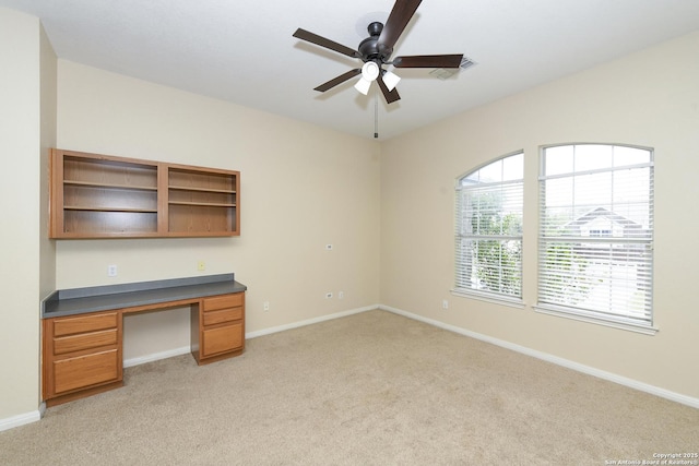 unfurnished office with built in study area, light colored carpet, ceiling fan, and baseboards