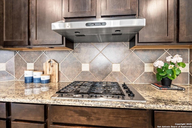 12627 Alamito Crk, San Antonio, TX 78254 - kitchen with stainless steel gas cooktop, under cabinet range hood, dark brown cabinets, tasteful backsplash, and light stone counters