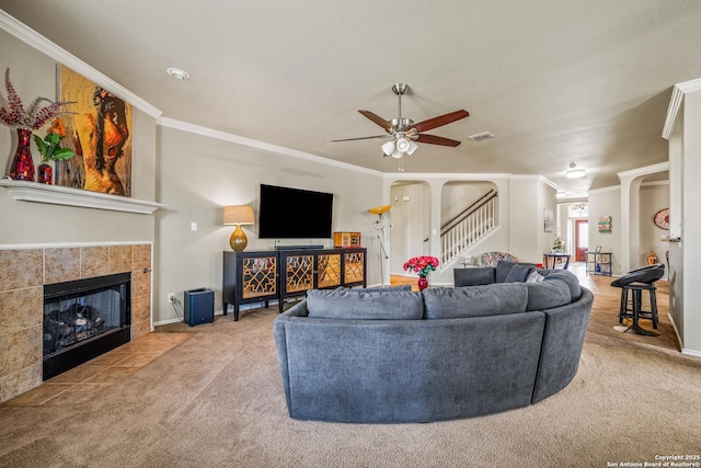222 Red Quill Nest, San Antonio, TX 78253 - carpeted living room featuring ceiling fan, stairs, ornamental molding, a tiled fireplace, and arched walkways