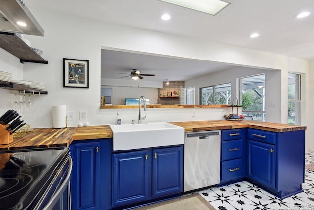 kitchen with wood counters, stainless steel dishwasher, a sink, blue cabinets, and recessed lighting